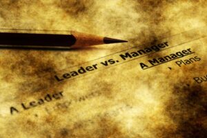 A pencil lays above text that reads "Leader versus Manager"
