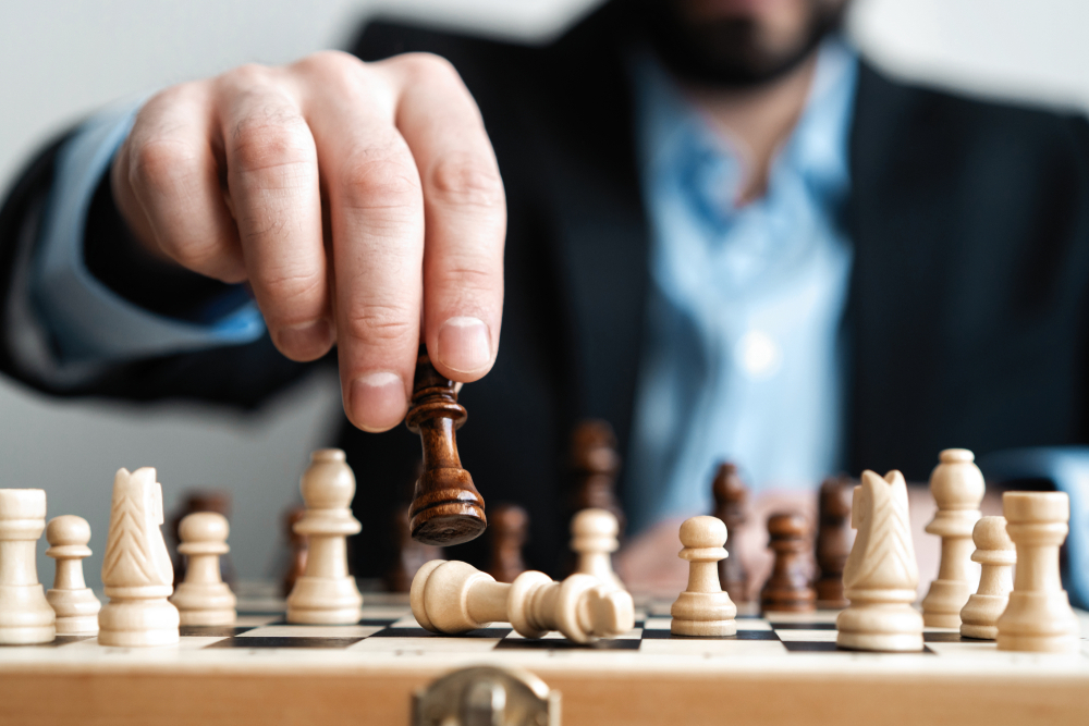 A businessman in a suit without a tie moves a piece on a chess board