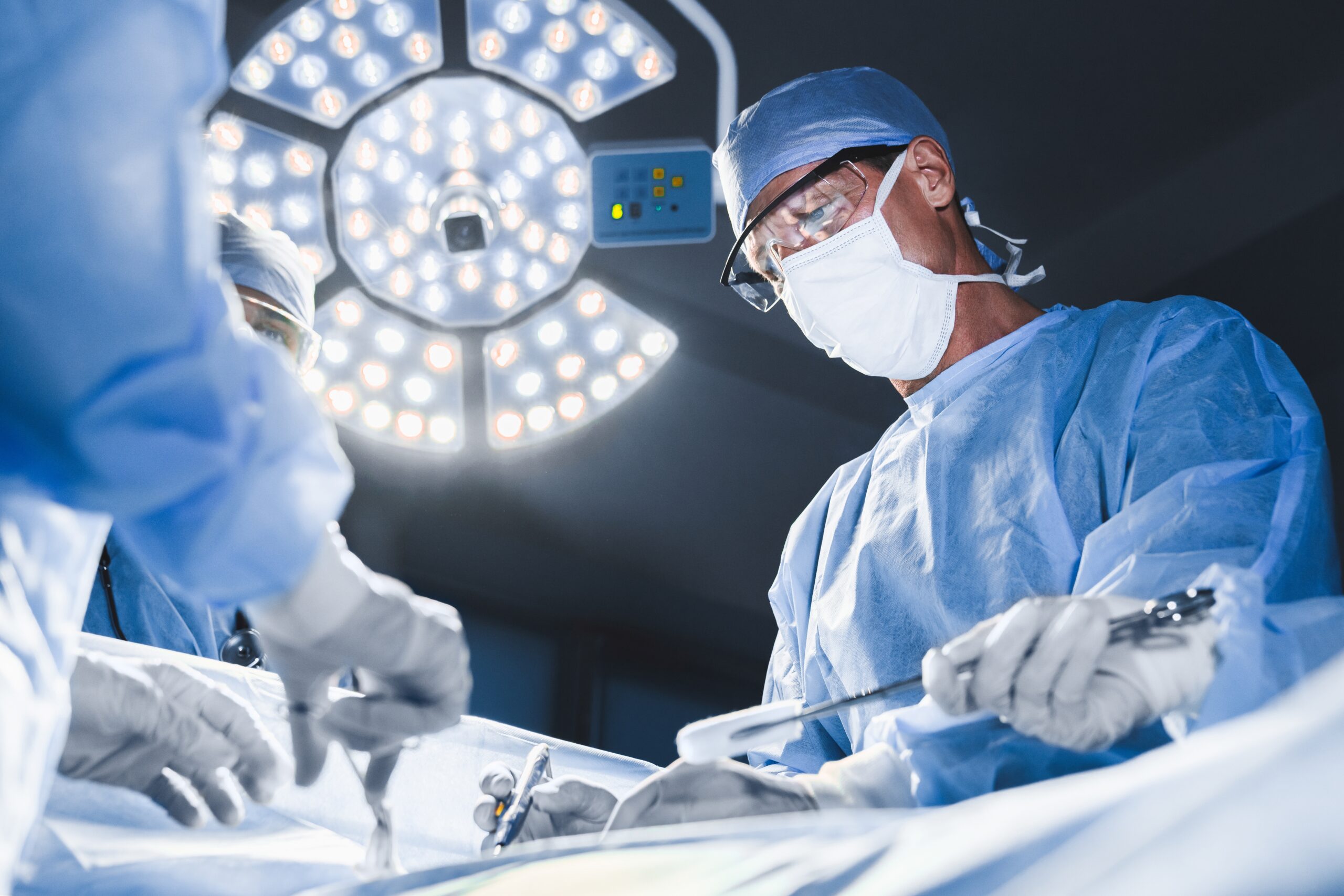 A group of surgeons in operating-room scrubs and mask perform a surgical procedure in an operating room at a hospital